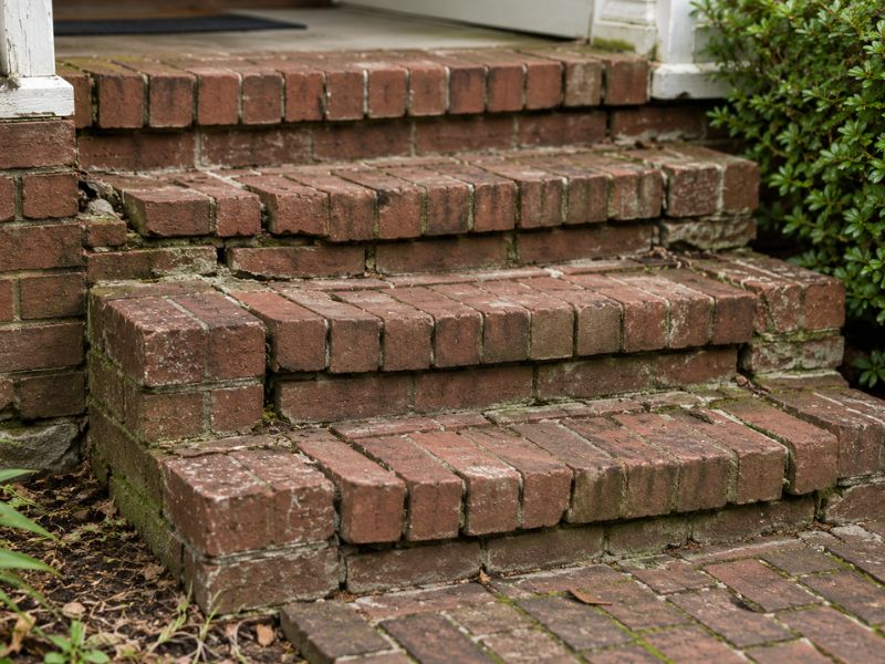 Loose and uneven brick steps with cracked mortar, shifted treads, and visible settlement near a home entrance in Auburn, Alabama.